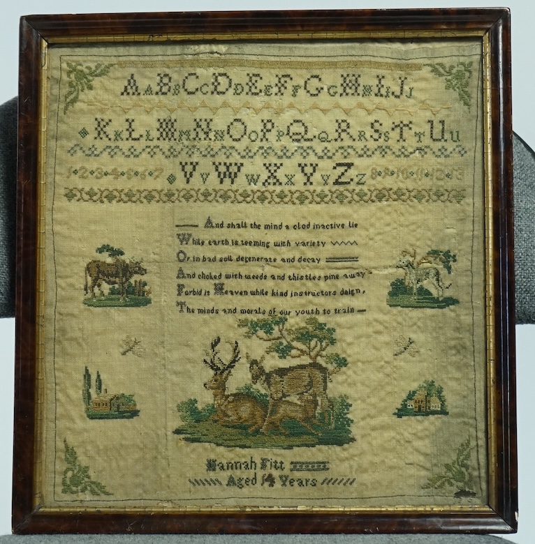 A Framed 19th century alphabet needlework sampler, by Hannah Fitt aged 14 years, (undated).worked with alphabet and numerals above a verse, surrounded by finely worked cartouche of a cow, dog, two houses and butterflies